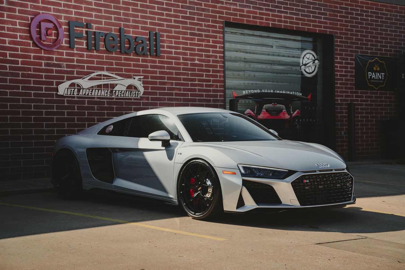 Silver Audi R8 parked in front of a brick building with a Fireball sign; a red car is visible inside.