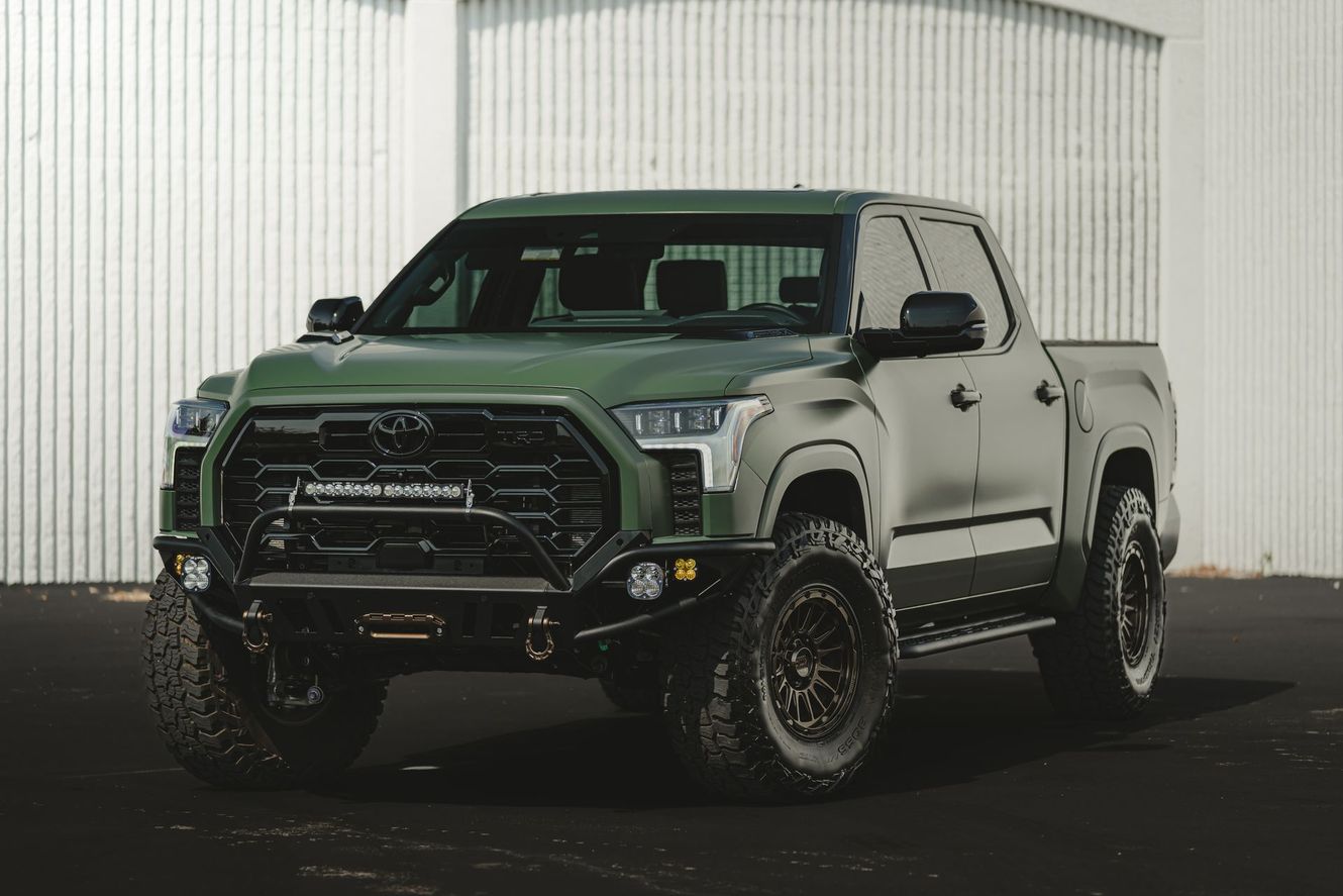 Green Toyota Tundra pickup truck with black modifications, parked in front of a white wall.