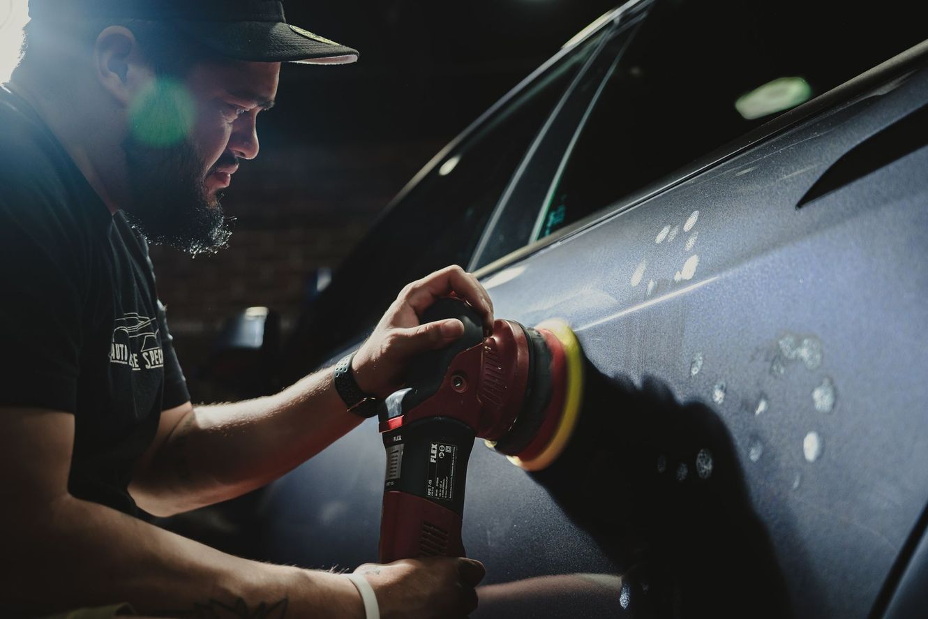 Man polishing a car, using a power buffer in a dimly lit garage.