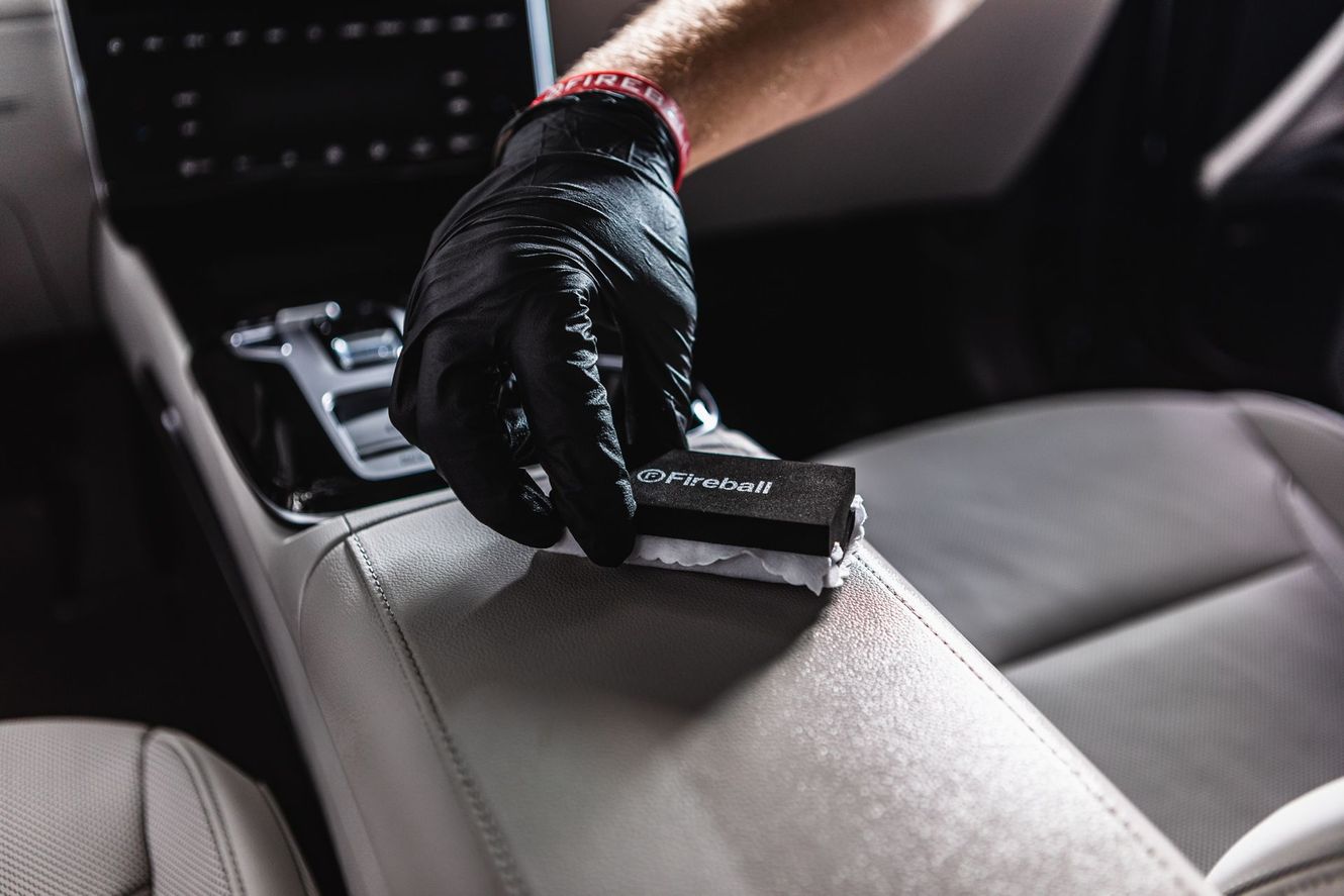 Person in black gloves applying ceramic coating to a car's light gray leather interior.