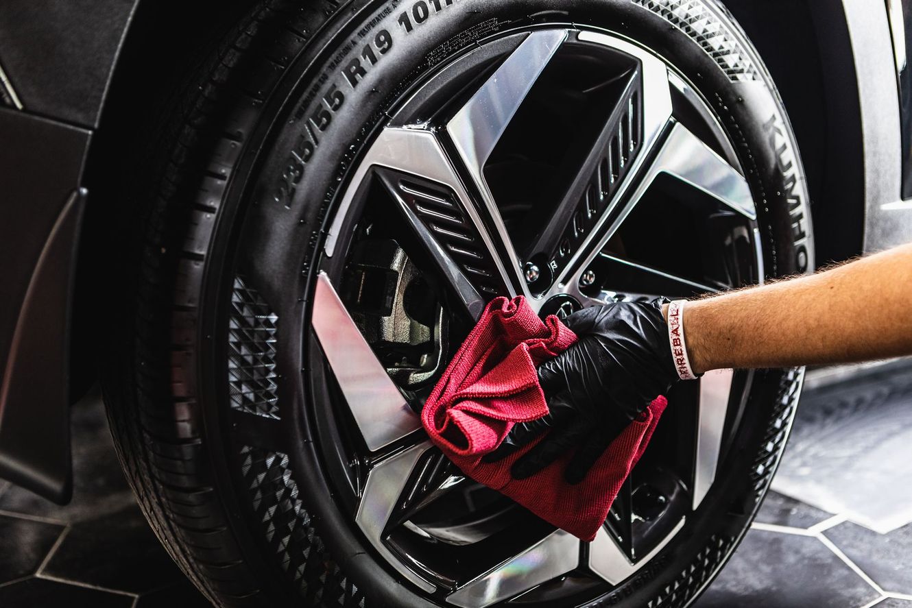 Person wearing a black glove wiping a car's shiny rim with a red cloth.