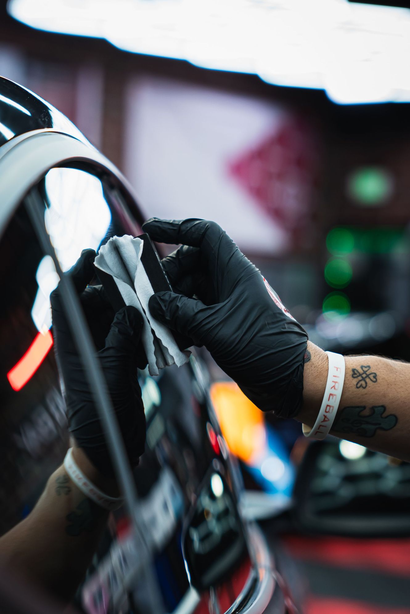 Person wearing black gloves applying a ceramic coating to a car's glossy black surface.