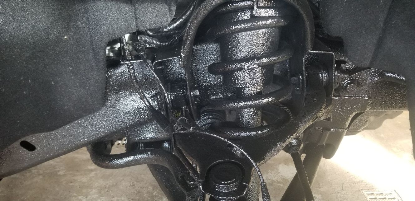 Close-up of a car's painted black suspension system with a spring and various arms.