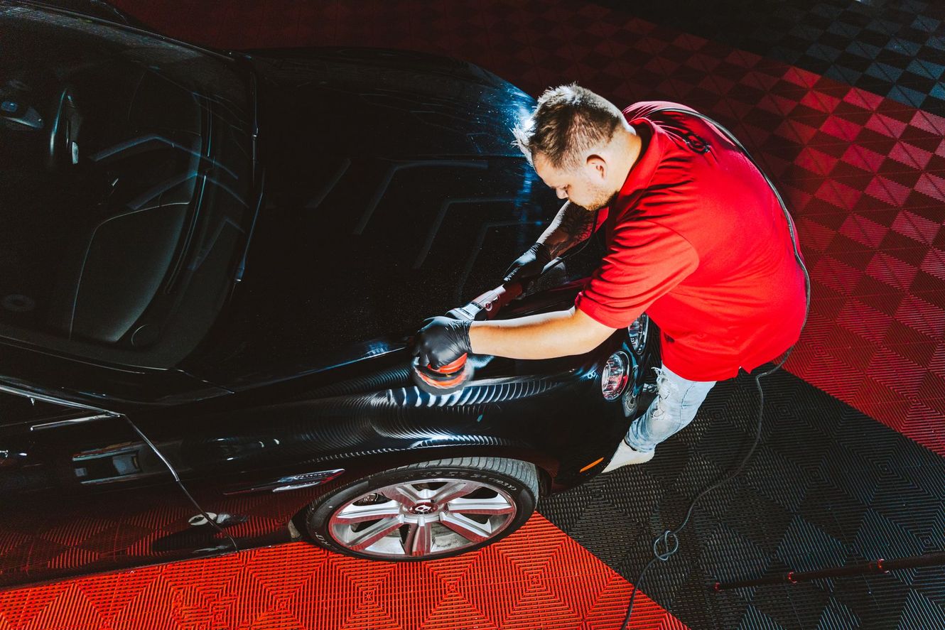 Man washing black car with sponge, on a checkered red and black floor.