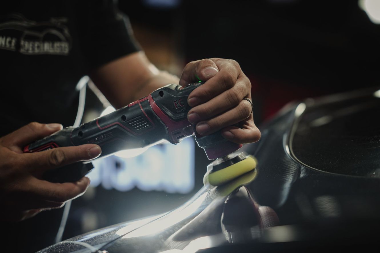 Person using a polisher on a car's body, applying detailing.