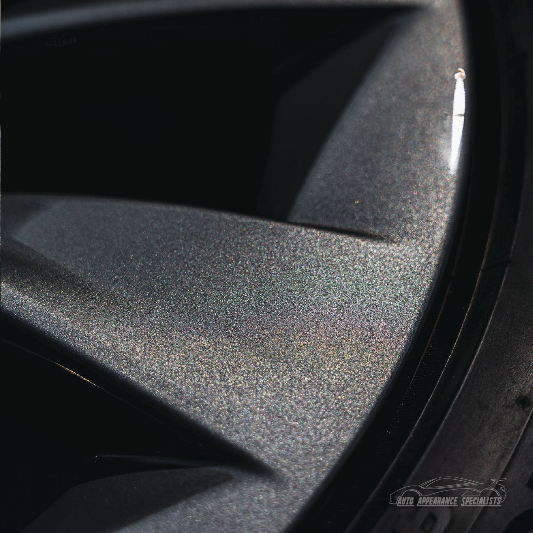 Close-up of a dark gray car wheel with subtle iridescent sparkle.