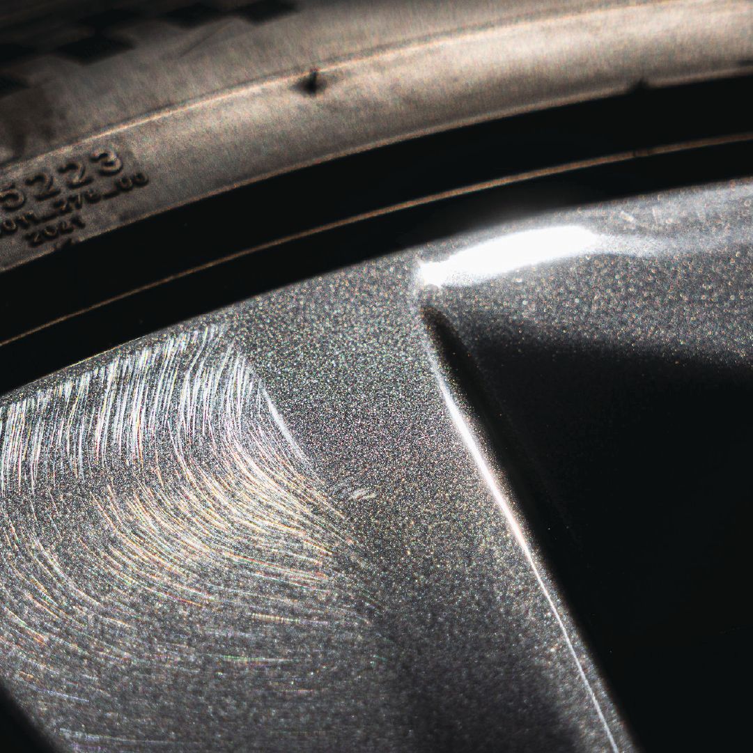 Close-up of a car's alloy wheel, showing scratches and wear, with a portion of the tire visible.