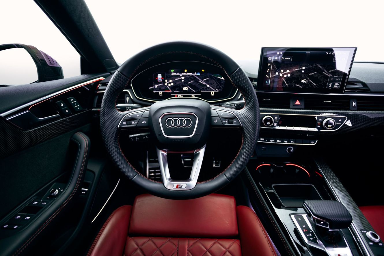Interior view of an Audi car with a steering wheel, digital display, and red leather seats.
