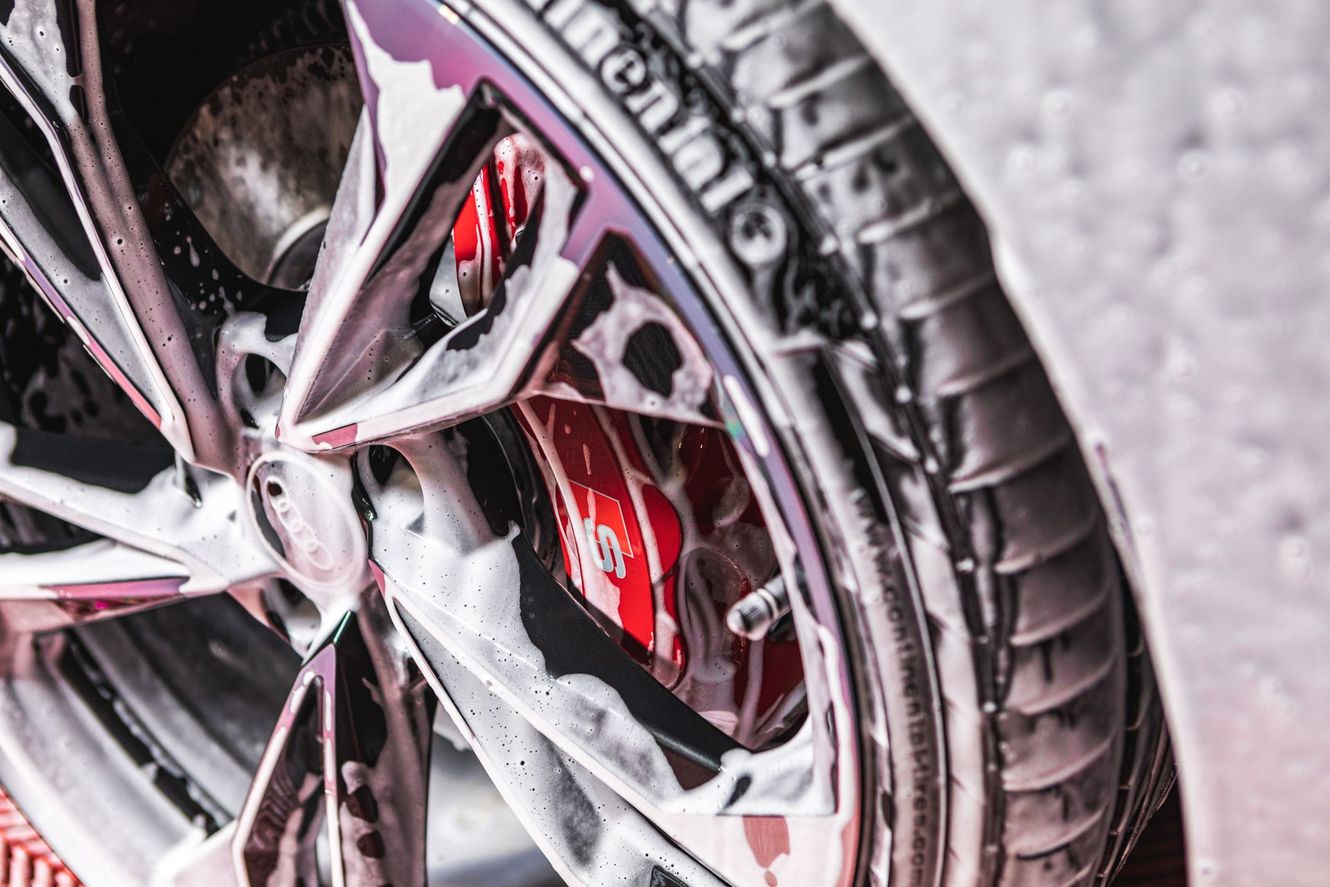 Car wheel with red brake caliper covered in foamy soap.