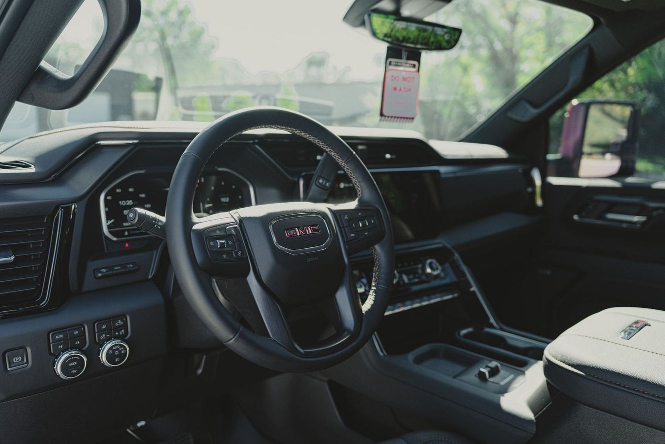 Interior of a GMC truck with a black dashboard, steering wheel, and center console; phone hanging from mirror.