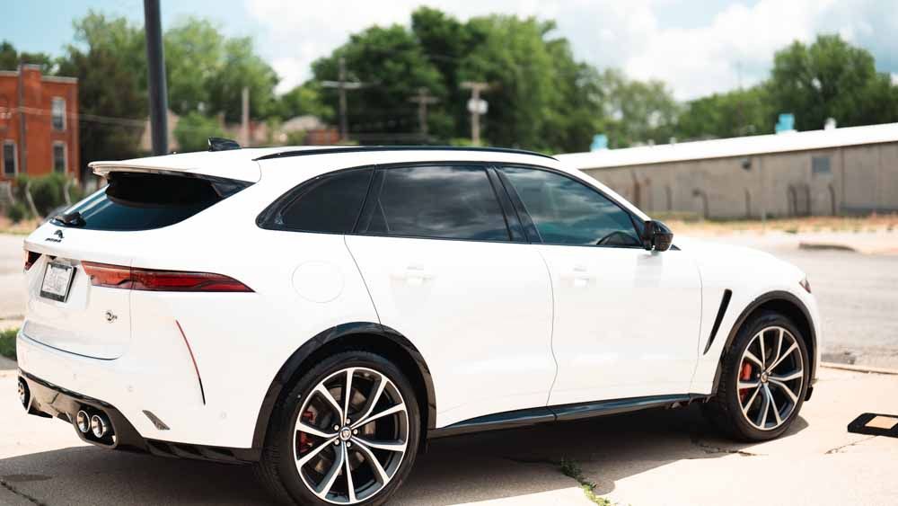White Jaguar F-Pace SUV parked on a city street, sunny day. Red brake calipers visible on wheels.