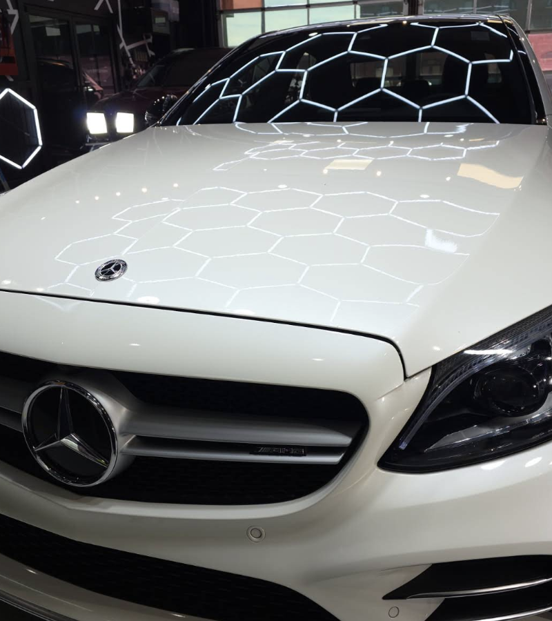 White Mercedes-Benz car with honeycomb pattern reflected on the hood. Front view, indoors.