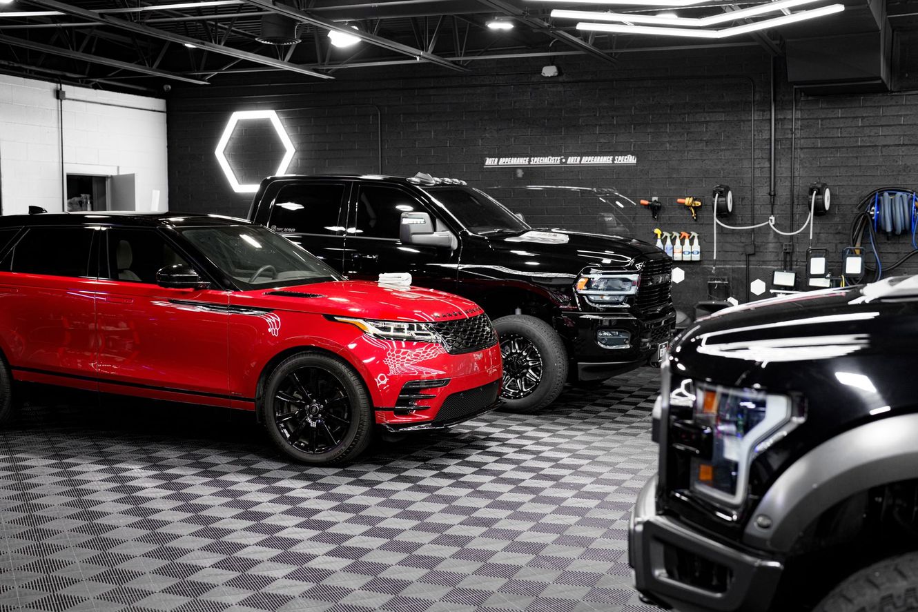 Red SUV, black truck, and black pickup truck parked in a detail shop.