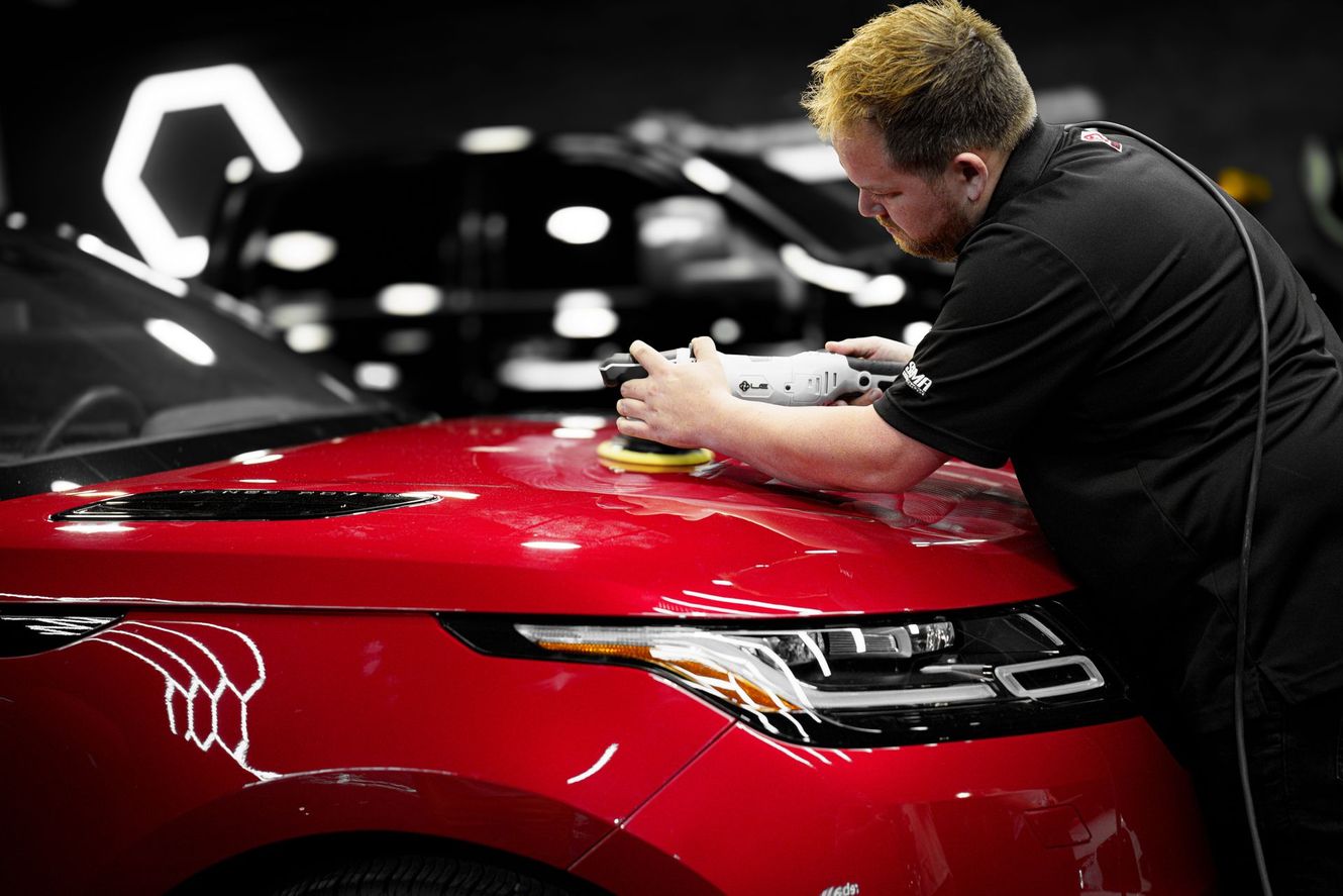 Person polishing a red car with a power polisher in a professional setting.