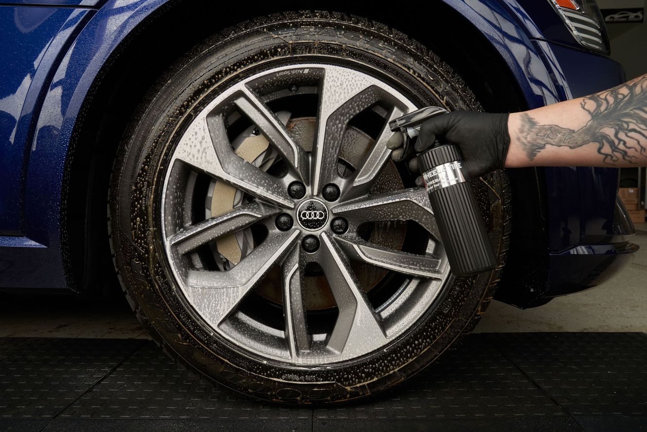 A person spraying a car tire with a cleaning solution, highlighting the wheel rim and tire.