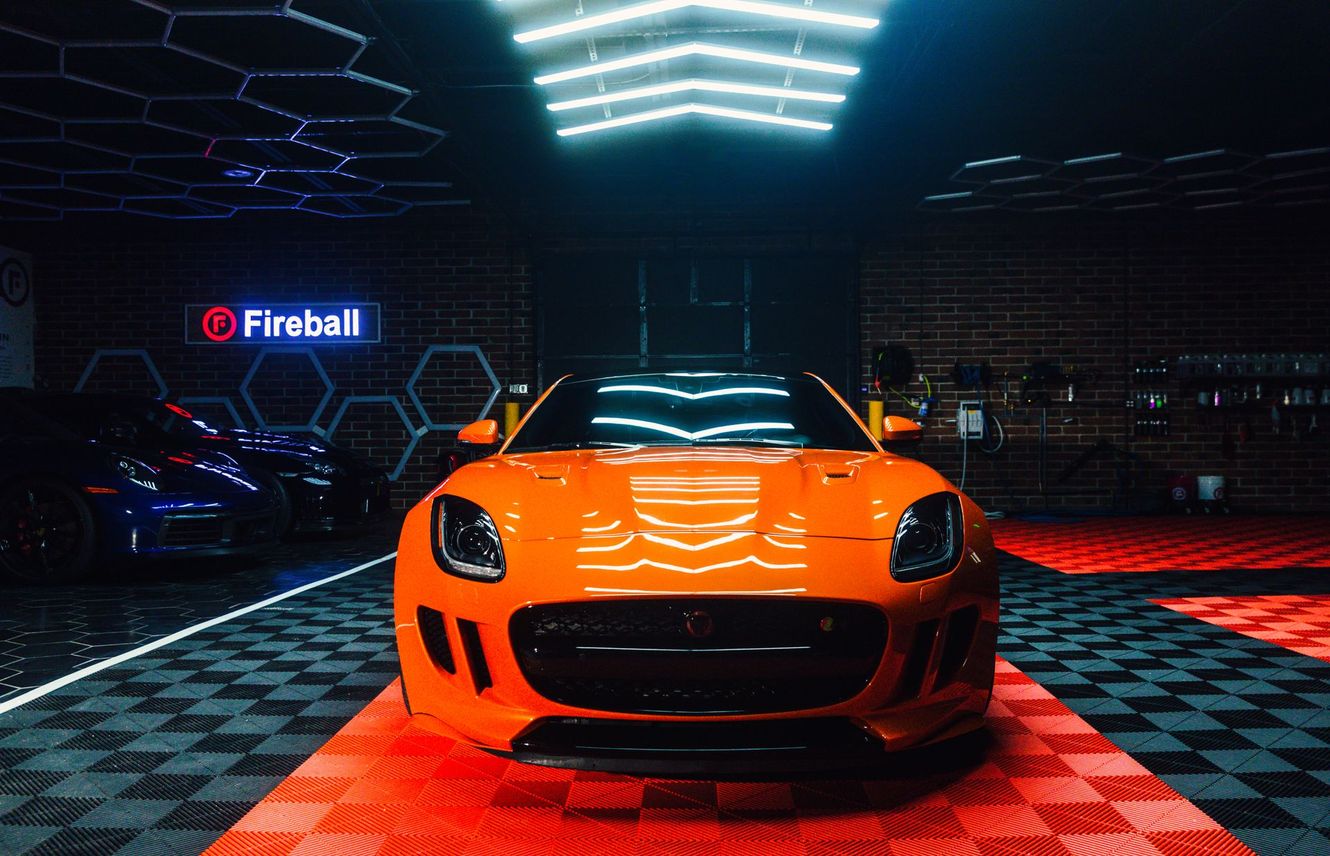 Orange sports car inside a garage with bright lights and brick walls, Fireball sign.