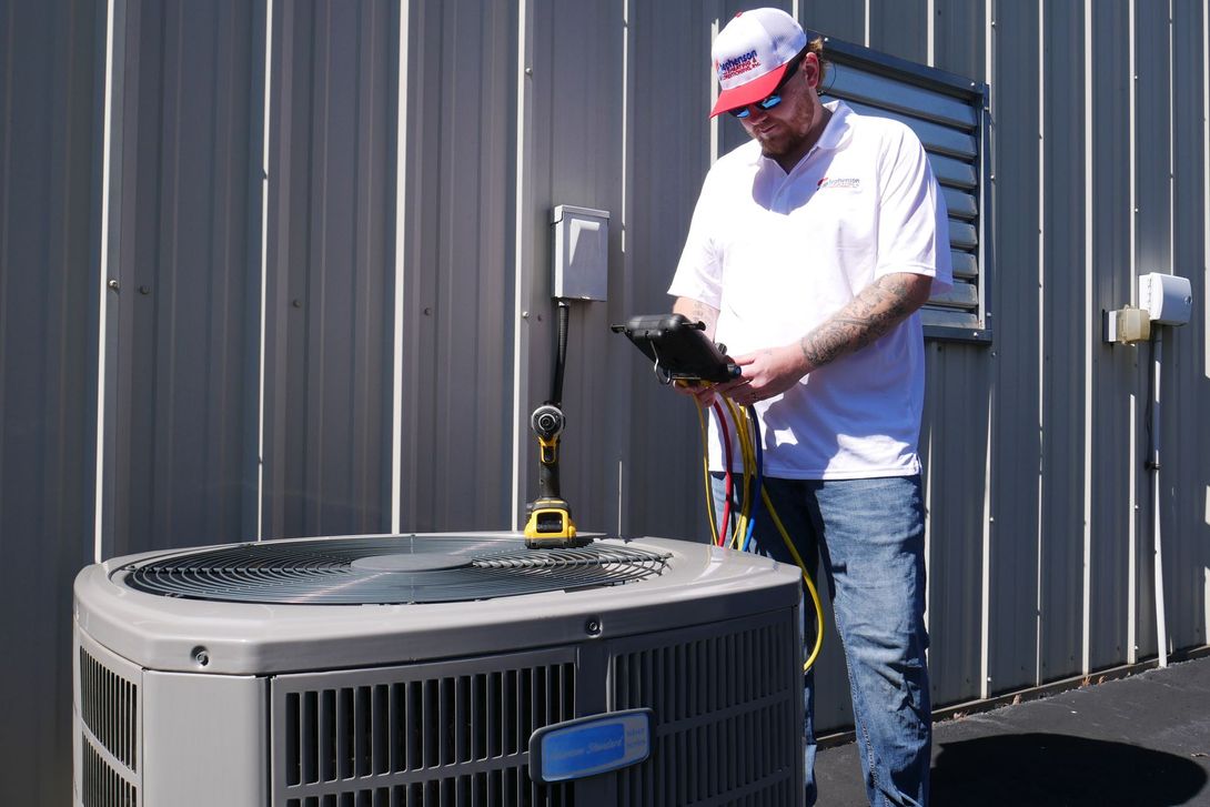 Technician inspecting an outdoor HVAC unit beside a building, using a clipboard and test meter.