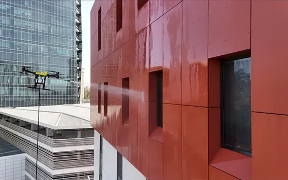 Drone spraying water on an orange building facade, near another glass skyscraper.