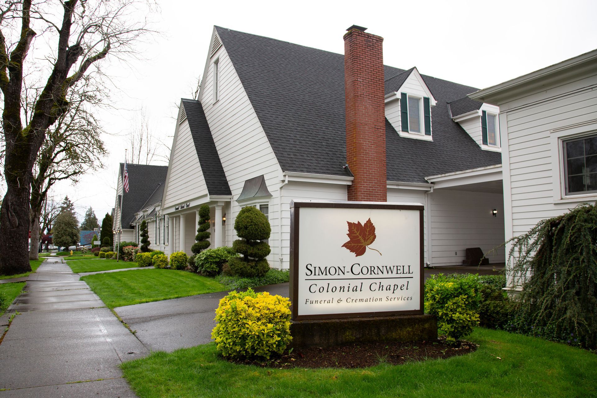 Sign for Smith-Cornwell Colonial Chapel with building in the background. Green lawn, sign with floral bed.
