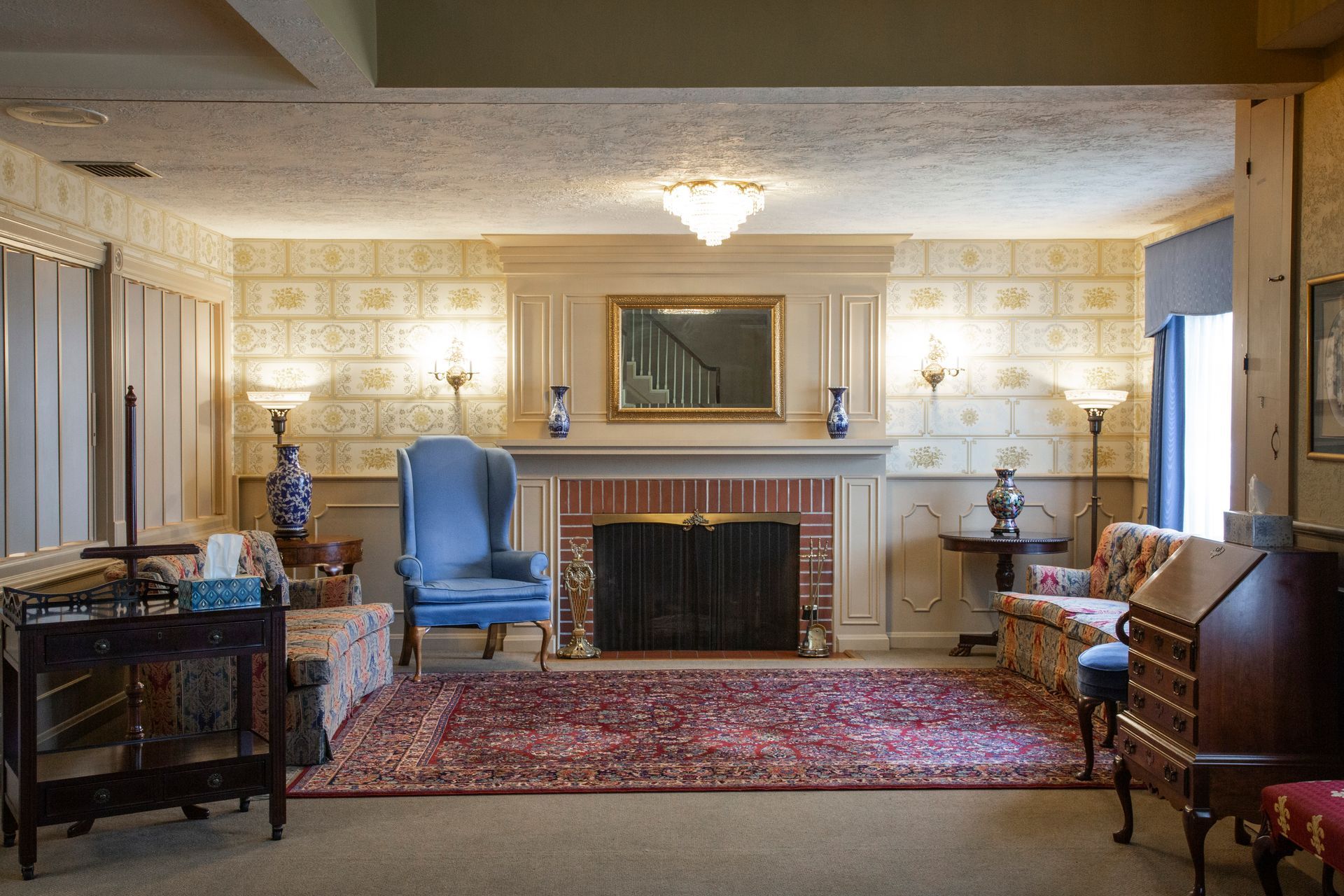 Elegant room with fireplace, chandeliers, patterned wallpaper, rug, furniture.