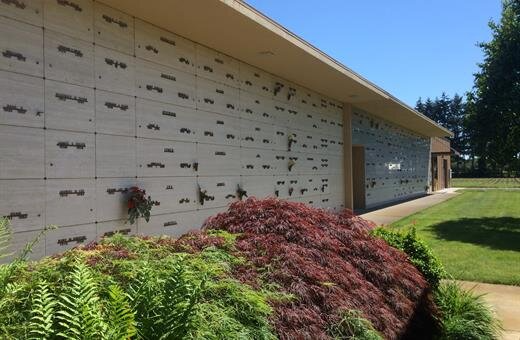 Exterior of a columbarium with rows of niches. Green plants and grass are in the foreground. Blue sky.