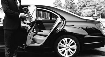 Person opening the door of a black luxury car on a driveway