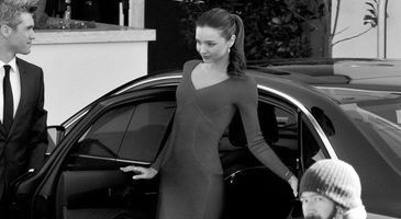 Person stepping out of a black car while another stands nearby; a child in a knit hat is in the foreground.