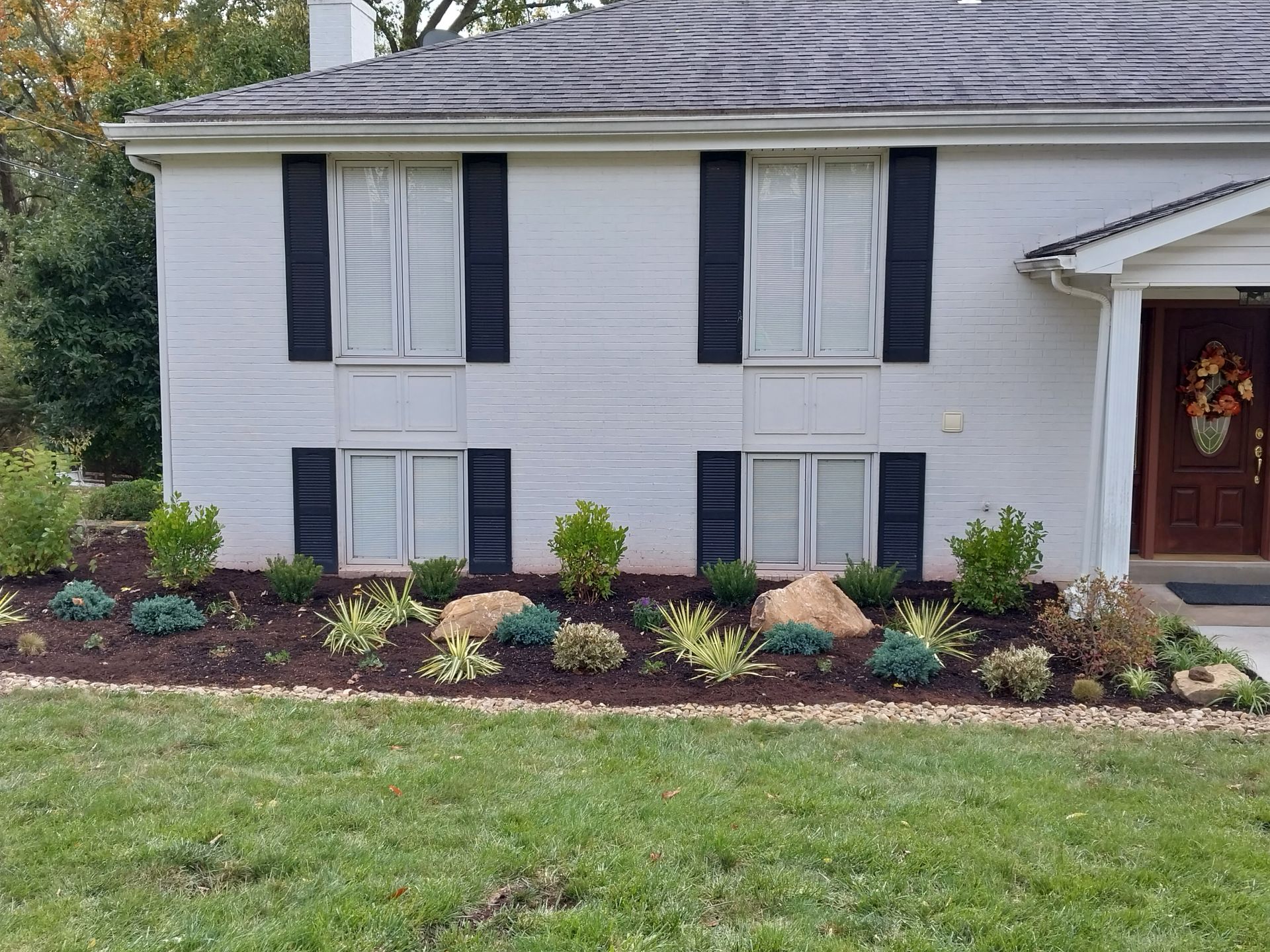 A white house with black shutters and a lush green lawn in front of it.