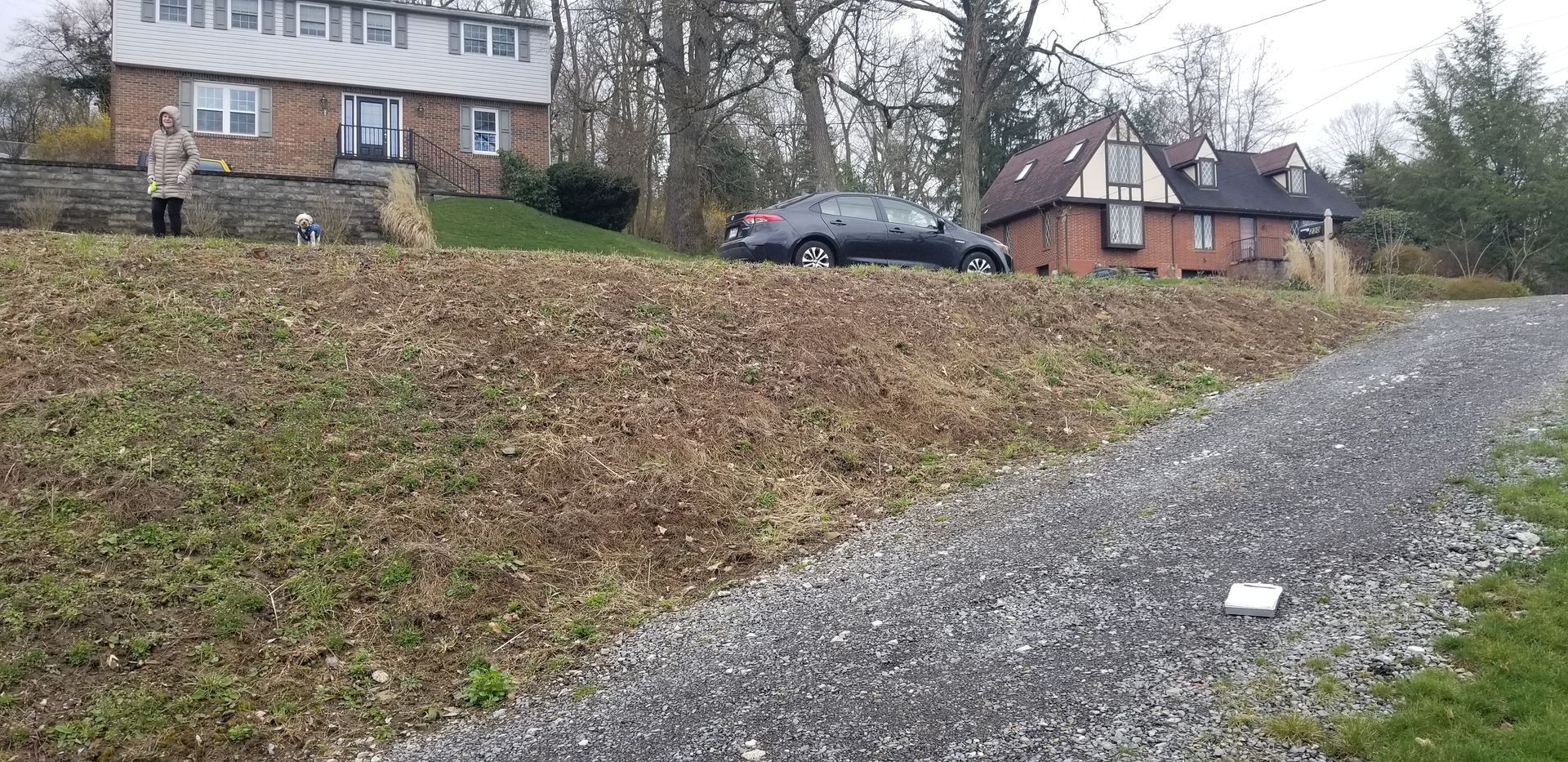 A car is parked on the side of a gravel road in front of a house.