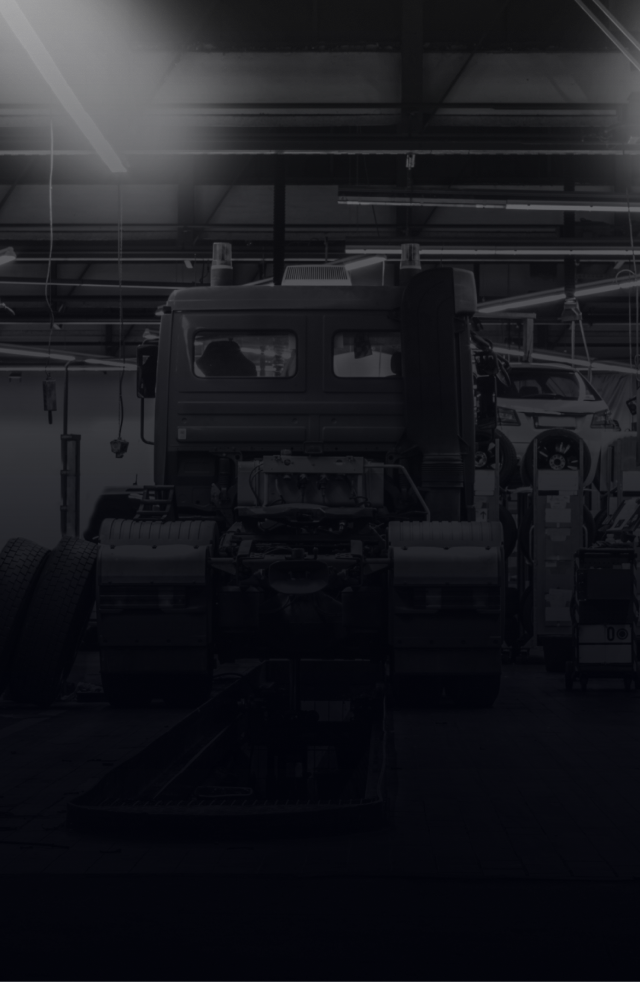 Truck chassis in a dimly lit garage; other vehicles visible in the background.