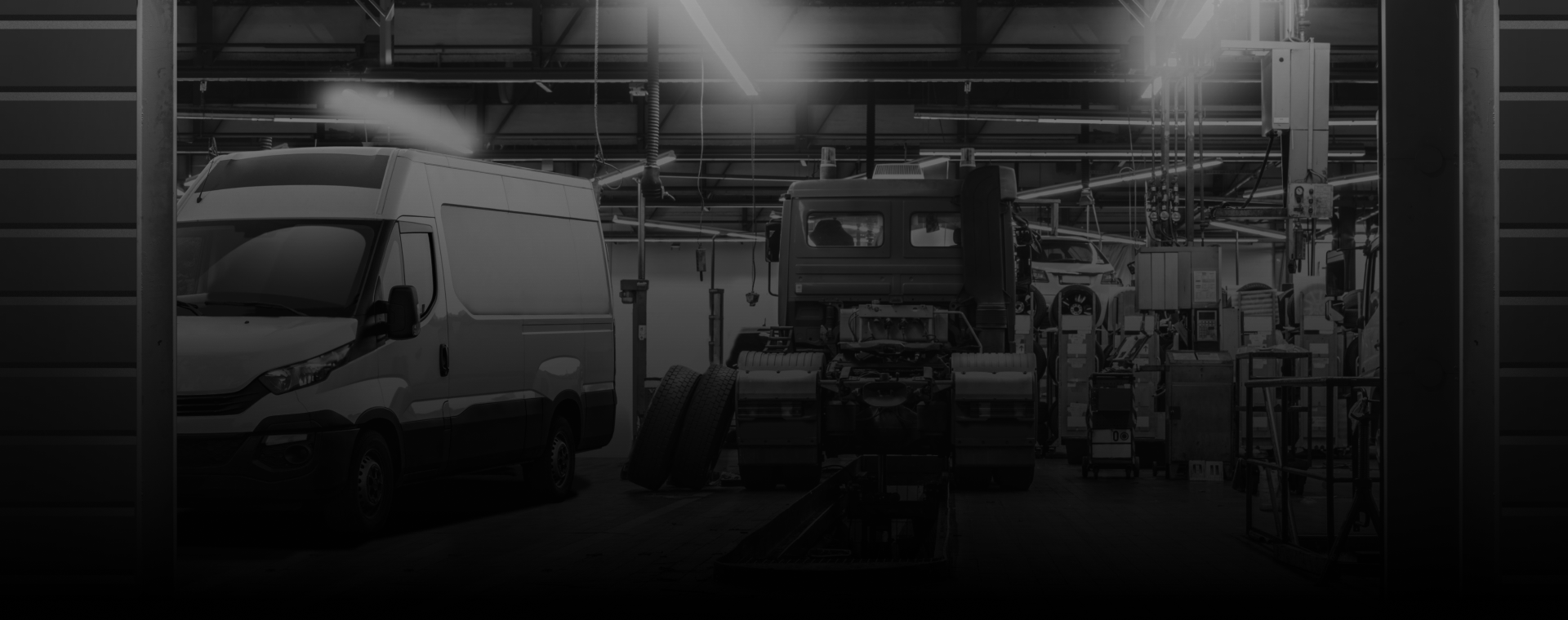 A grayscale view inside a vehicle manufacturing plant with trucks and a van.