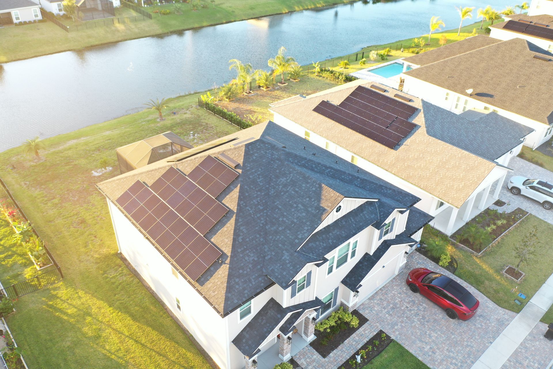 Aerial view of two houses beside a river, with solar panels and a red car in the driveway.