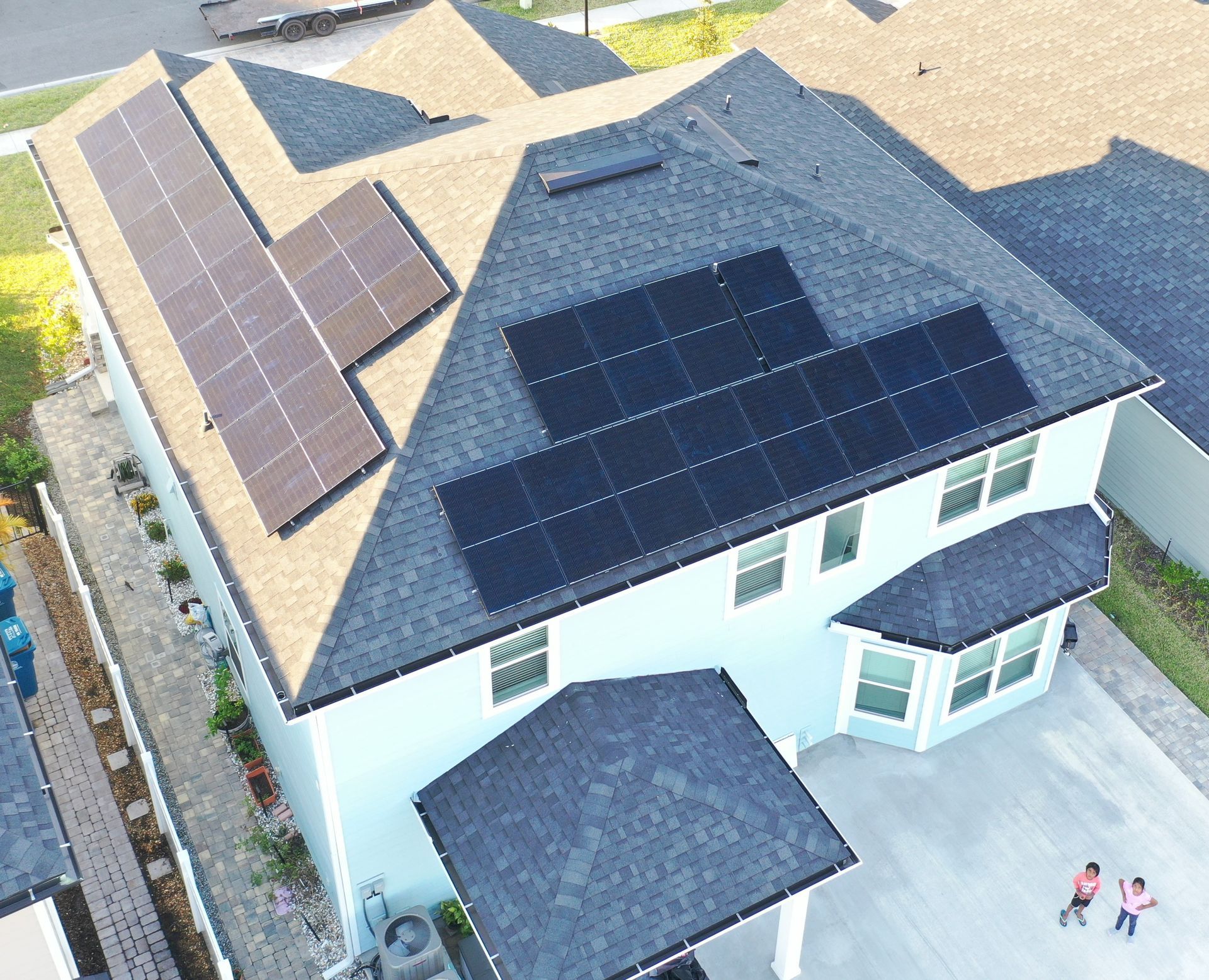 Aerial view of a house with dark solar panels on the roof and two people standing in the driveway