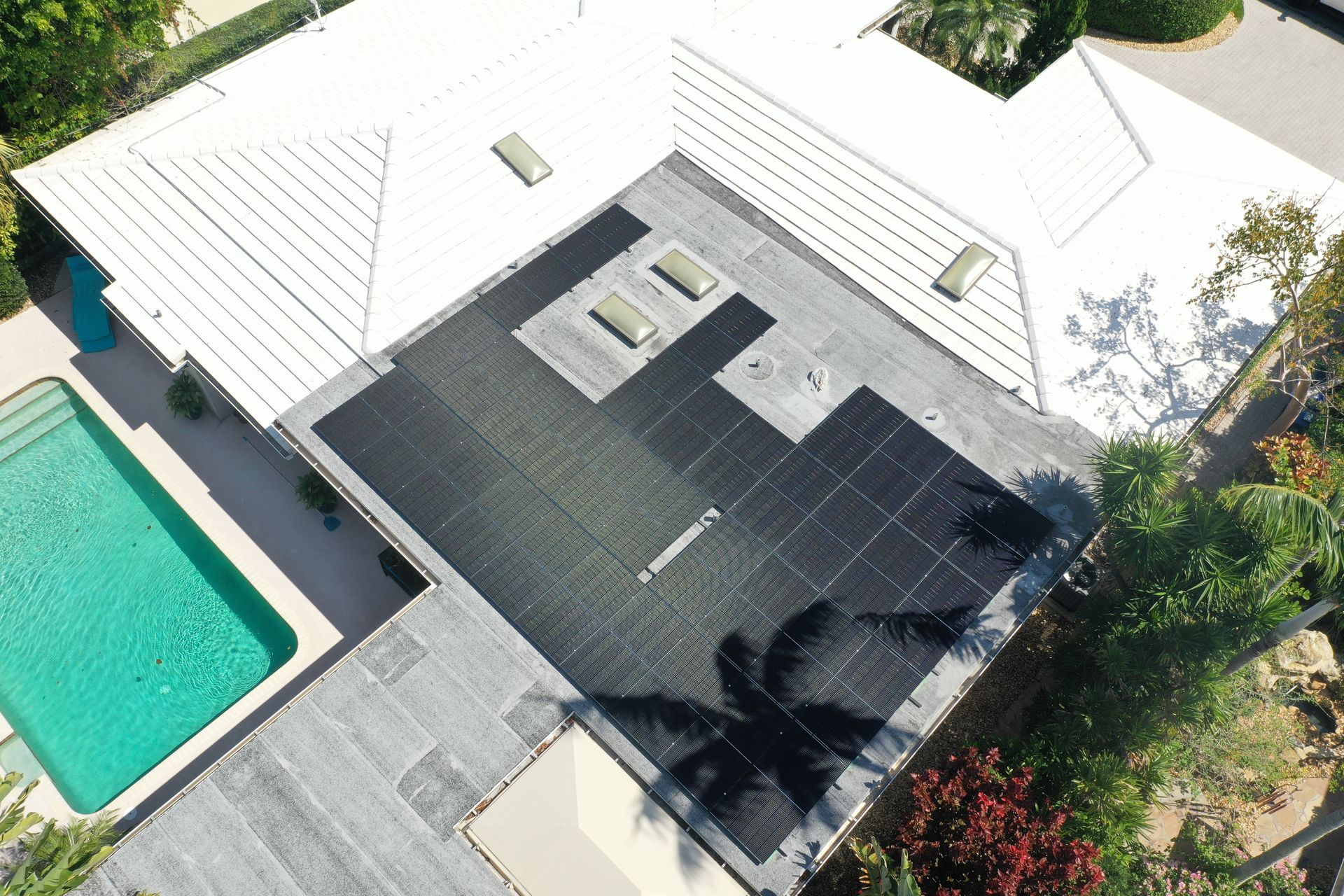 Aerial view of a modern house with a dark roof, white walls, and a turquoise swimming pool.