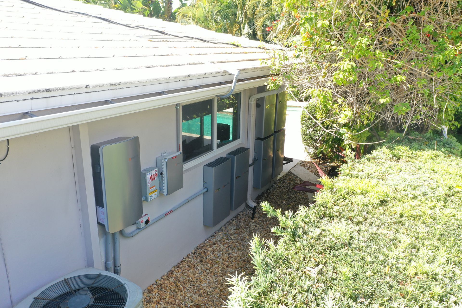 Side view of a house with utility meters, a window, and shrubs along the exterior wall.