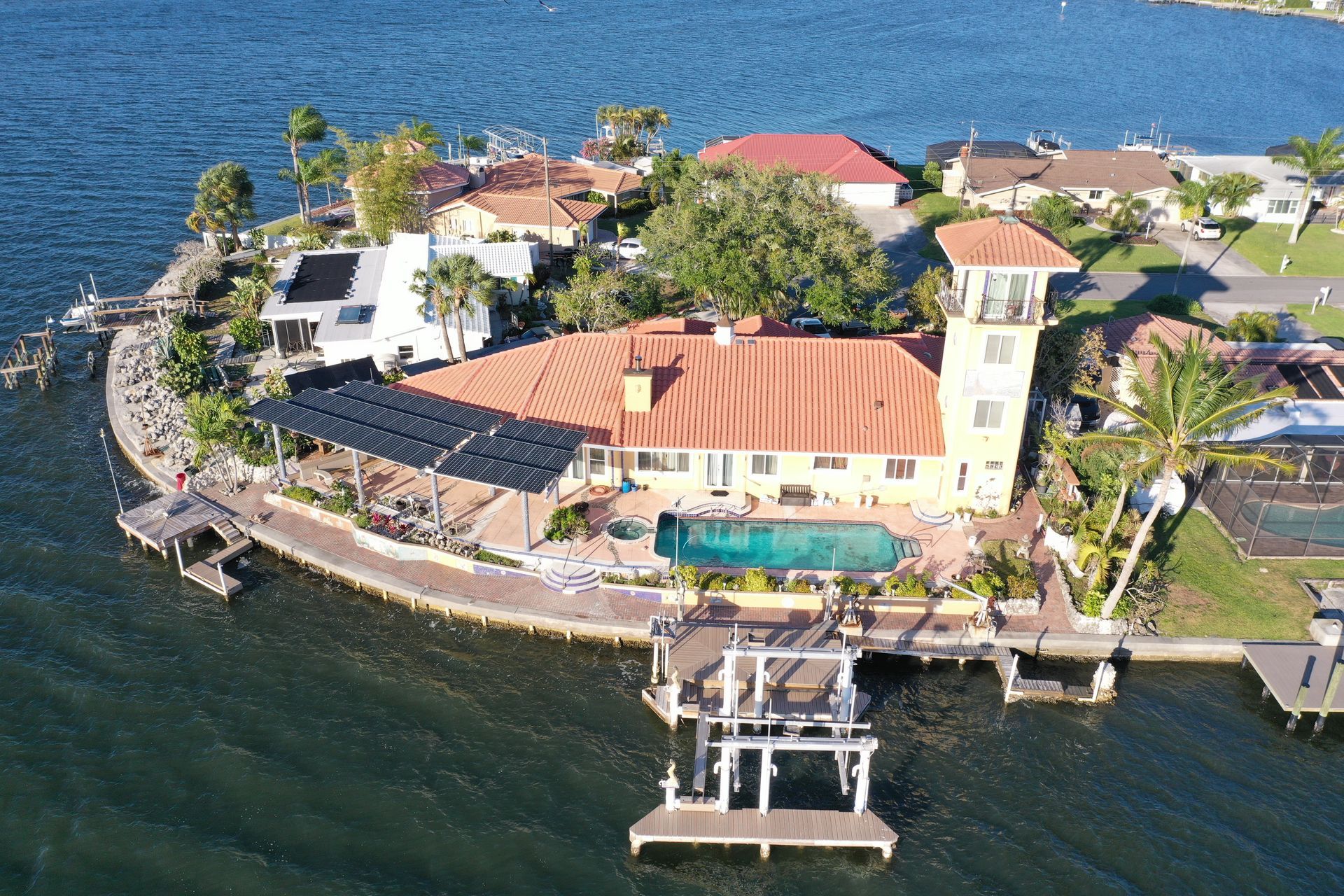 Aerial view of a waterfront resort with terracotta roofs, pool, docks, and surrounding blue water.