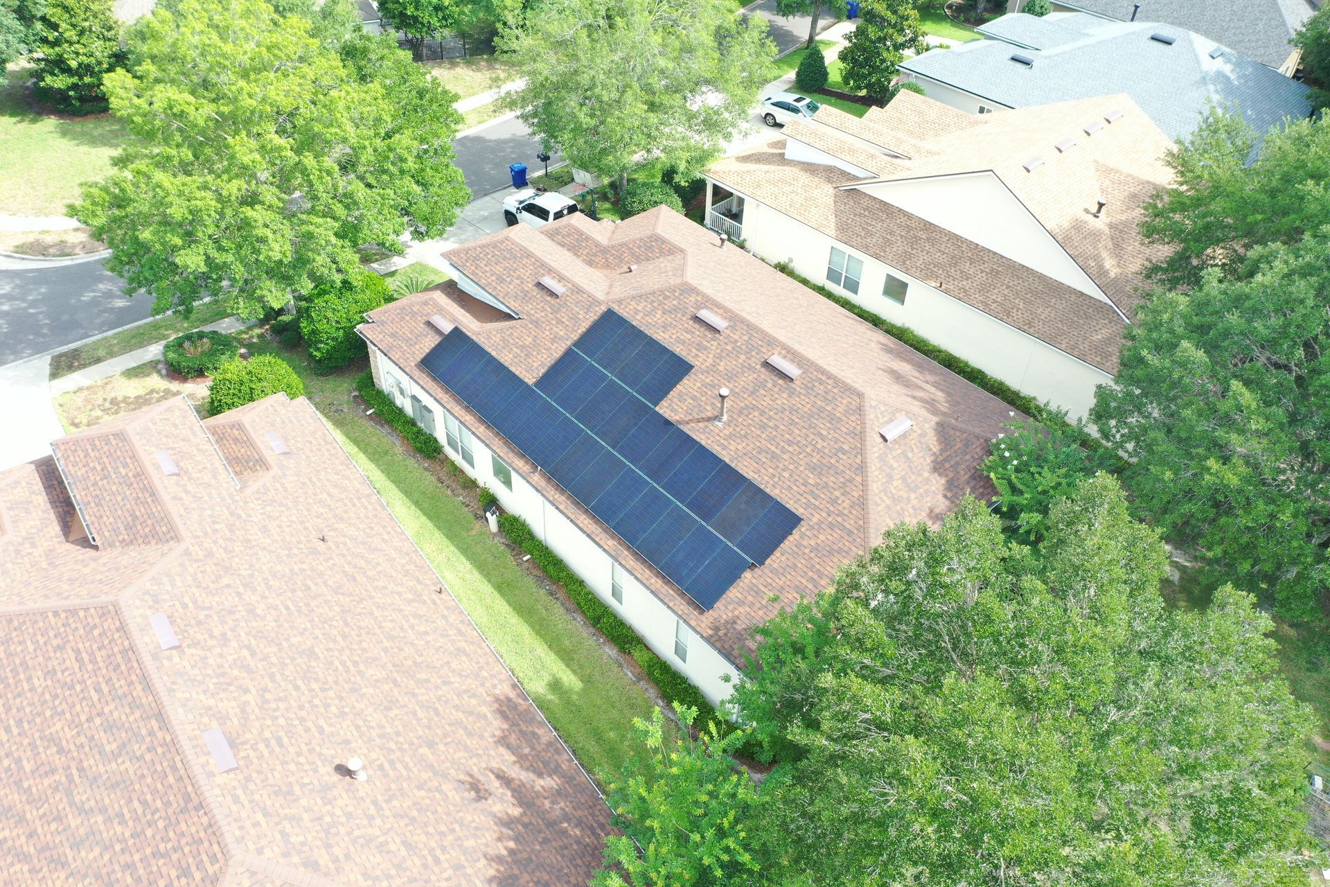Aerial view of a house with rooftop solar panels surrounded by trees and neighboring homes