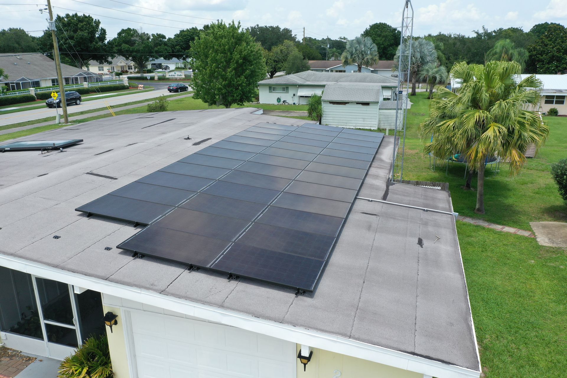 Rooftop solar panels on a light gray building, with a grassy yard and trees nearby.