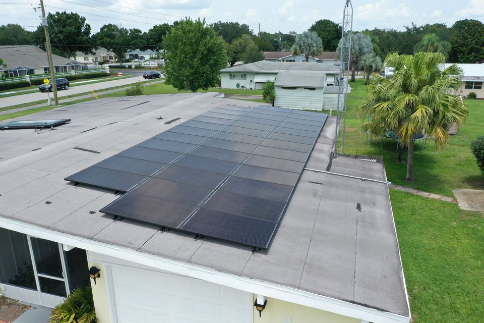 Worker in orange safety gear installing solar panels on a rooftop under a clear blue sky.