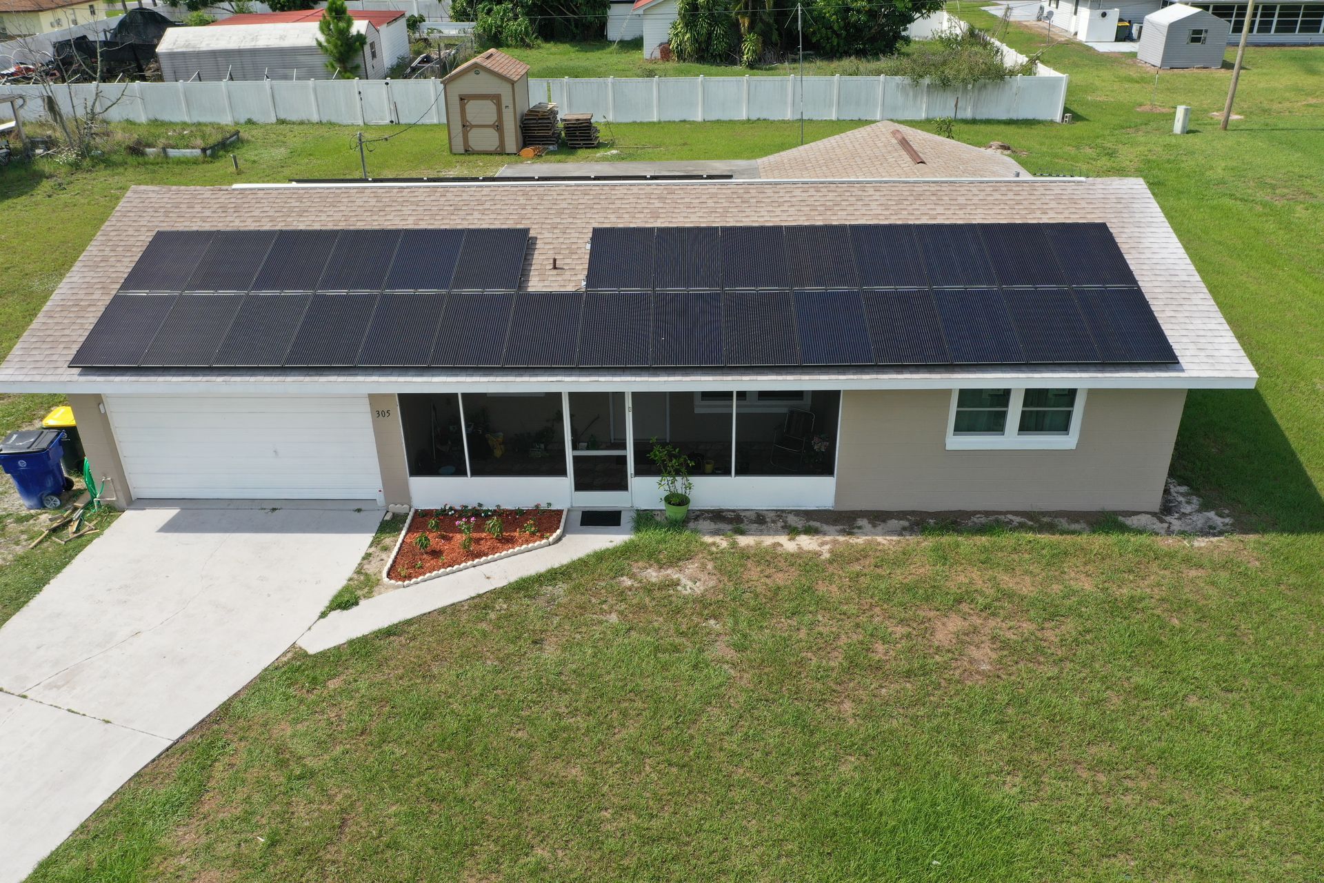 Aerial view of a single-story house with solar panels and a front yard.