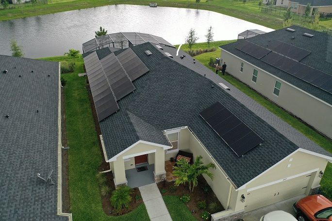 Aerial view of a suburban house with rooftop solar panels beside a pond and neighboring homes