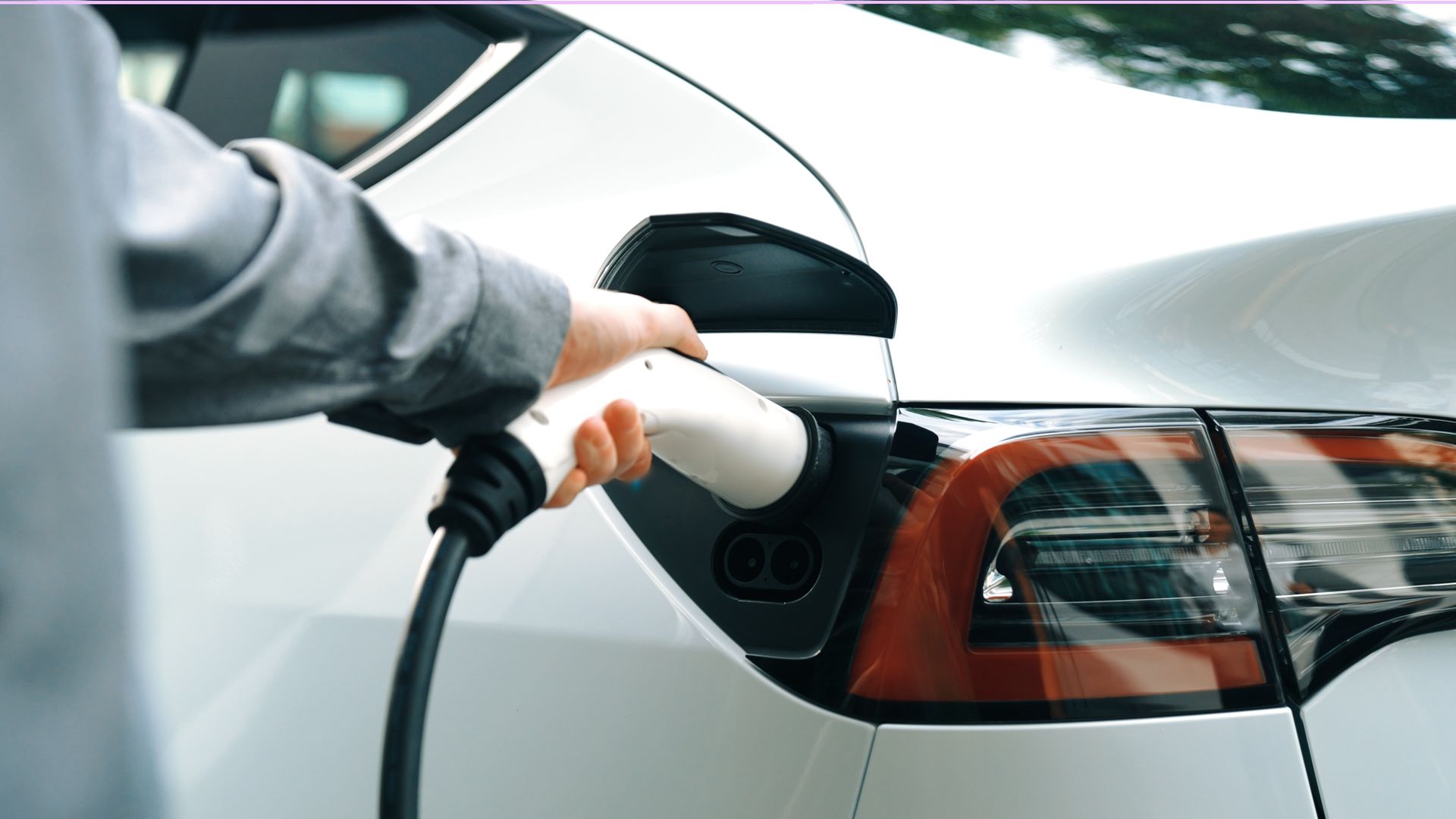 Hand plugging an electric vehicle into a charging port on a white car