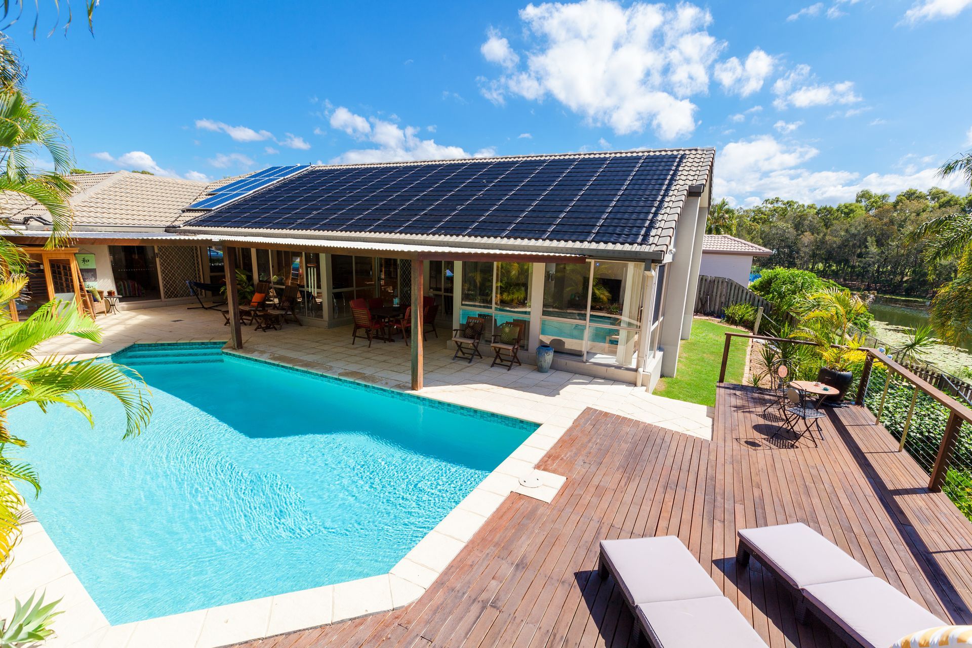 Modern villa with solar panels, a turquoise pool, and a wooden deck under a blue sky