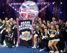 Cheering cheer squad holding National Cheerleading Association grand national champion banner on stage
