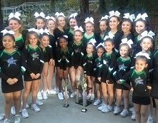 Cheerleading team posing together in black and green uniforms, holding trophies and medals outdoors