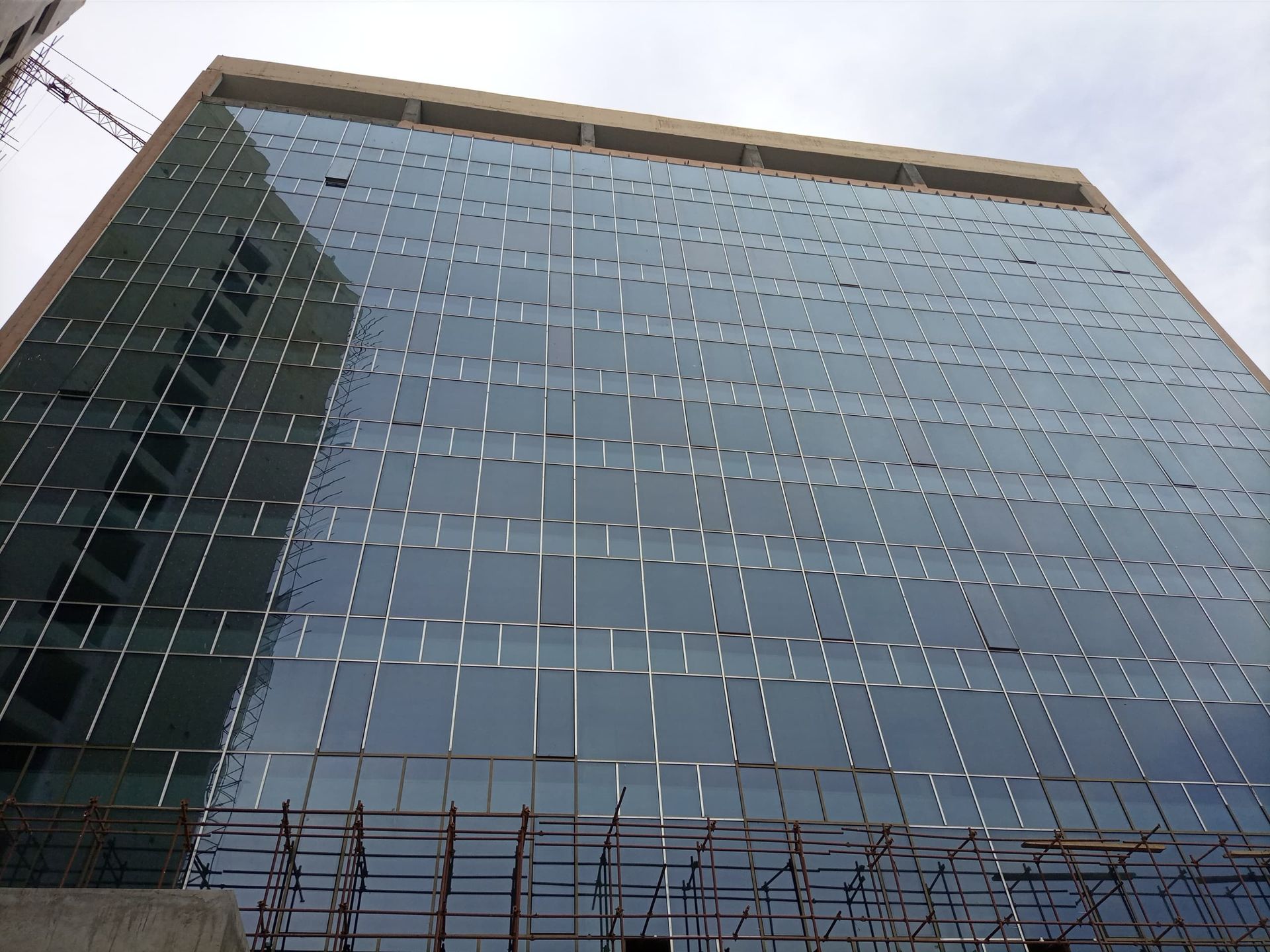 Glass-walled office building under construction; scaffolding at base.