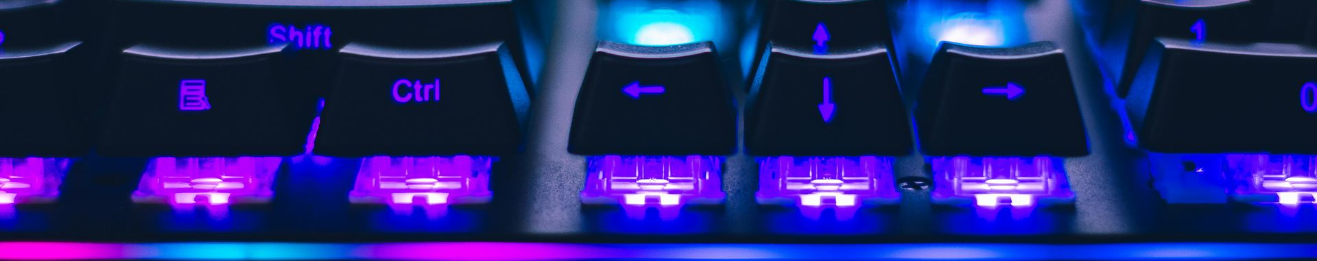 Primer plano de un teclado mecánico retroiluminado con luces moradas y azules.