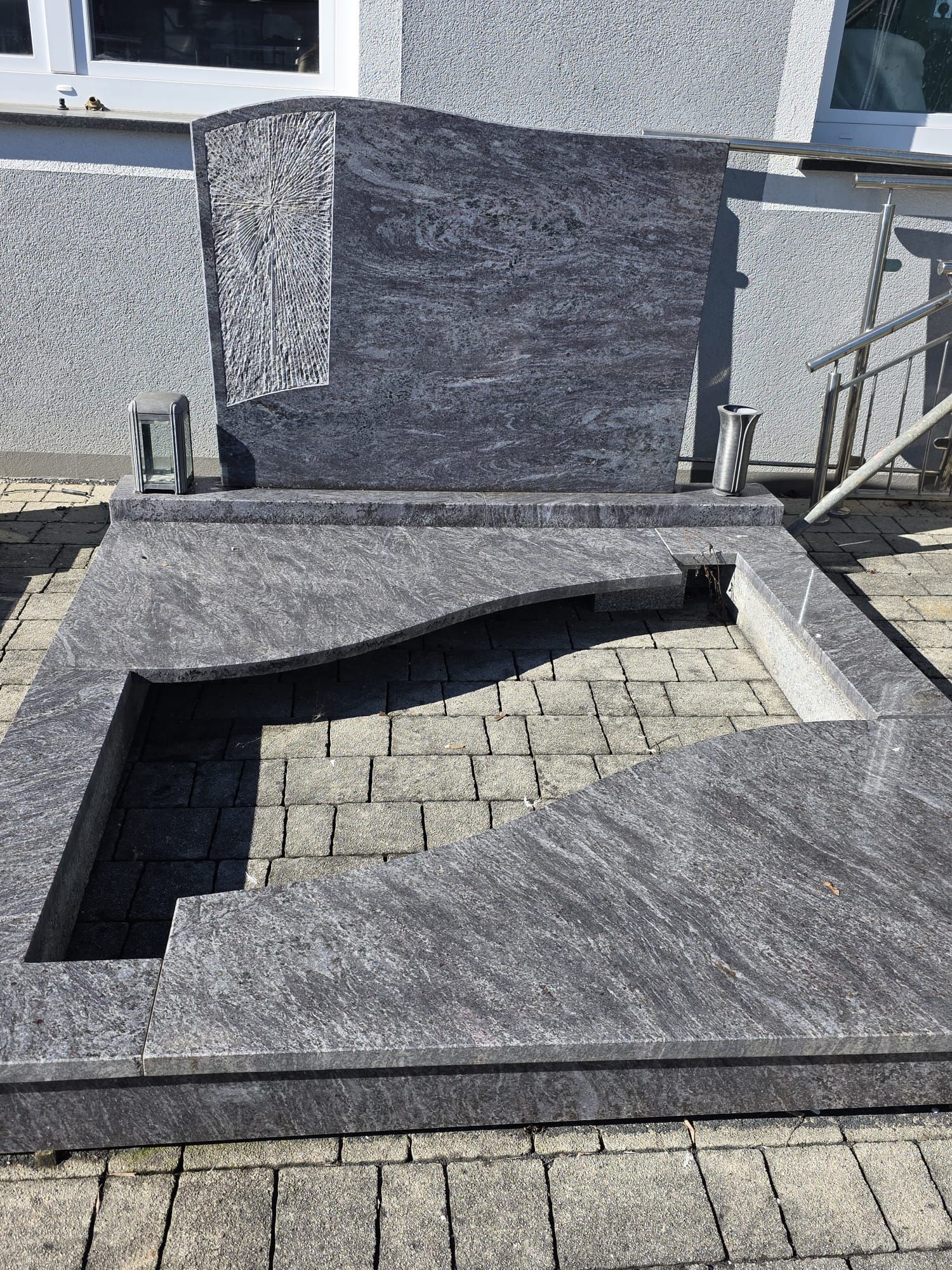 Gedenkbrunnen aus Granit mit flachem rechteckigem Becken und erhöhtem Mittelblock auf einem gepflasterten Innenhof.
