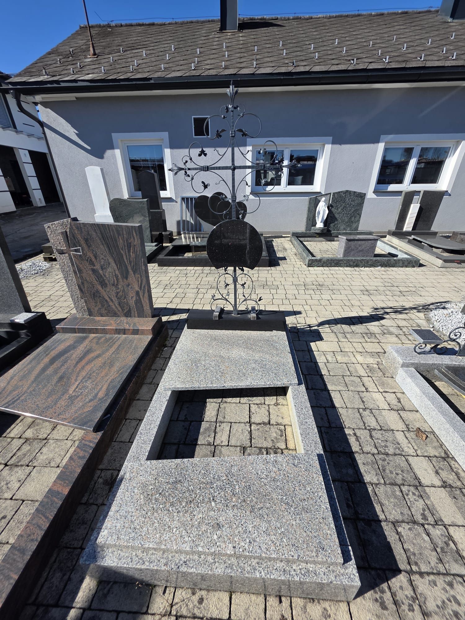 Steinterrasse mit zentraler Feuerstelle vor einem grauen Haus im hellen Sonnenlicht