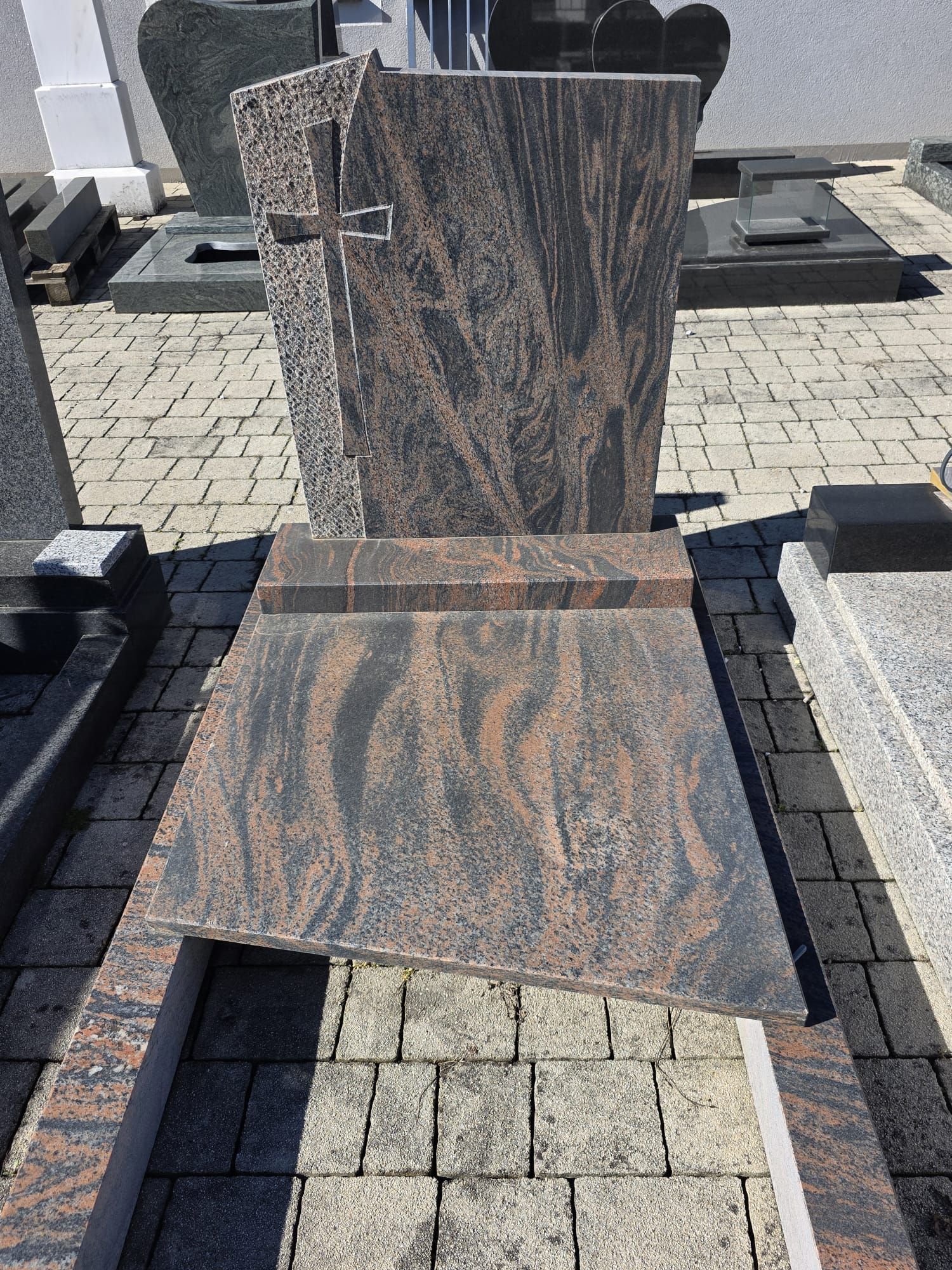 Gedenkgrab aus Granit mit poliertem, aufrechtem Grabstein und schrägem Sockel auf einem gepflasterten Friedhof.